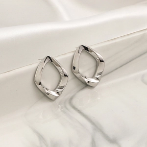 Minimalist silver geometric twisted hoop earrings displayed on white silk and marble
