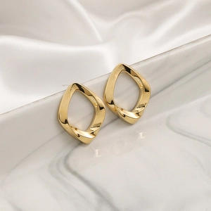 Minimalist geometric gold twist earrings on marble and silk background