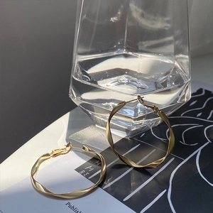 Classic gold twisted geometric hoop earrings displayed on a magazine with artistic shadows