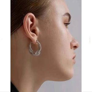 Close-up of silver geometric spring earrings with detailed pleated texture on a model