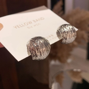 Close-up of silver C-shaped earrings featuring a molten lava textured metallic surface