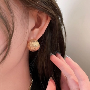 Close-up of golden dome stud earring with fine brushed metal texture on ear