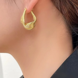 Elegant gold geometric spring earrings with spiral metal texture on a female model