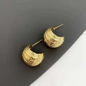 Golden C-shaped stud earrings with textured bark finish on a dark grey leather background