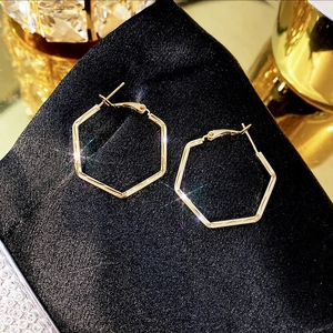 Macro shot of gold geometric hexagonal hoop earrings on luxurious black silk fabric