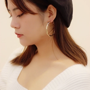 Detailed close-up of large golden twisted rope hoop earrings on model with beret
