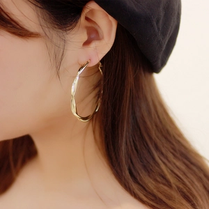 Close-up of elegant gold twisted hoop earrings with a glossy mirror finish on model