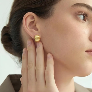 Minimalist gold-plated brushed metal stud earrings shown worn on a model's ear