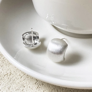 Minimalist brushed silver stud earrings with a sleek semicircular design on ceramic