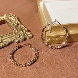 Golden mosaic geometric hoop earrings with textured metallic facets on velvet