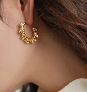 Detail of chunky gold hoop earring with twisted texture and cylindrical metal accents