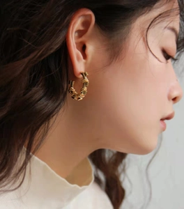 Detailed close-up of textured gold-plated geometric hoop earring worn by a model
