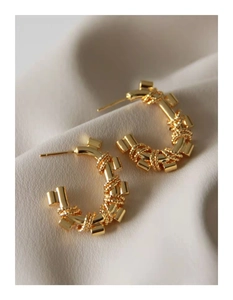Detailed close-up of golden geometric C-shaped earrings with spiral textured metal pattern