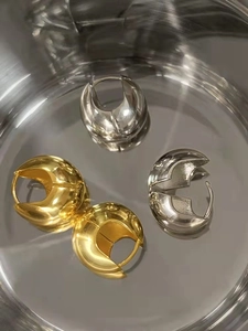 Close-up of high-polish gold and silver teardrop earrings on reflective surface