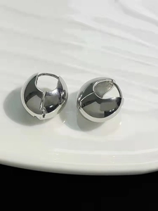 Macro shot of polished silver teardrop earrings on a white wave-textured ceramic plate