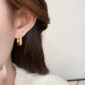 Detail of gold U-shaped earring with embossed letters worn by a model in white tweed