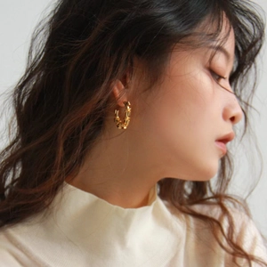 Minimalist gold bamboo texture hoop earrings worn by a model in a high-fashion portrait