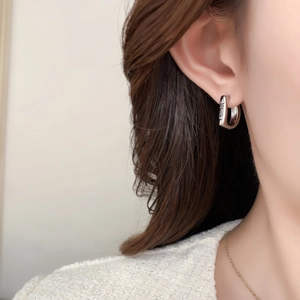 U-shaped silver metal hoop earring with NE engraving shown on a female model