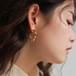 Elegant gold-plated geometric hoop earrings with textured weave design on model
