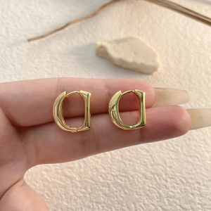 Polished gold D-shaped letter hoop earrings held between fingers for size reference