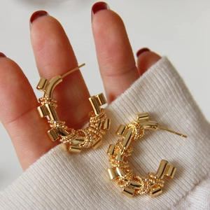 Golden woven hoop earrings with 18K textured finish held against knitwear background