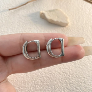 Detail of silver D-shaped metal hoop earring with high-polish finish on a textured background