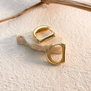 Polished gold D-shape hoop earrings displayed on a natural stone with wood branch