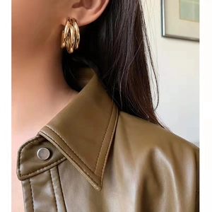 Boucles d'oreilles C dorées multicouches polies portées avec une veste en cuir vert