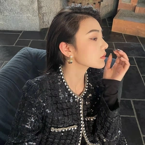 Elegant black tweed jacket with sequins and gold C-shaped pearl earrings on a model