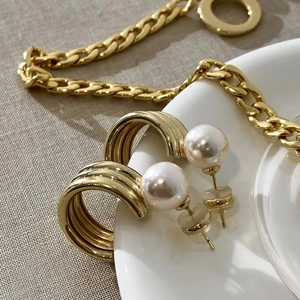 Elegant C-shaped golden metal hoop earrings with round white pearls on a white plate