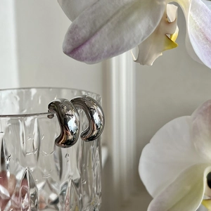 Gepolijste zilveren geometrische oorbellen aan een glasrand met witte orchideeën