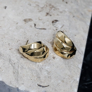 Macro detail of 14K gold plated layered ribbon earrings on a natural stone surface