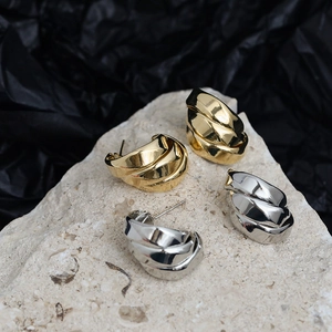 Detailed view of layered C-shaped gold and silver earrings on textured stone