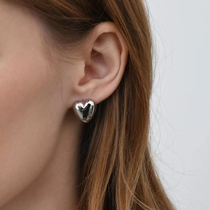 Minimalist silver heart stud earrings with polished metallic finish on a female model