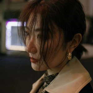 Close-up of golden rhombus wave textured hoop earrings worn by a model in a city night setting