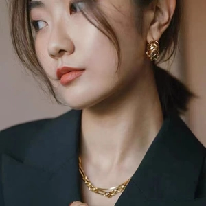 Detail of model wearing gold braided hoop earrings and layered rectangular chain necklace