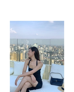 Elegant black halter dress paired with a navy crocodile texture shoulder bag on a balcony