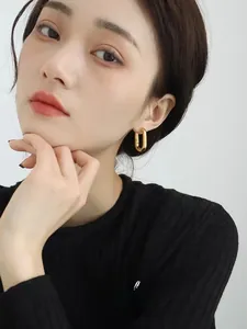 Close-up of geometric 14K gold brass U-shaped hoop earrings on a model with glossy finish