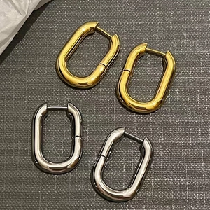 Polished 14K brass U-shaped hoop earrings in gold and silver set on leather surface