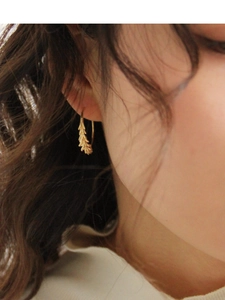 Detail of gold wheat ear hoop earrings worn by a model in soft lighting