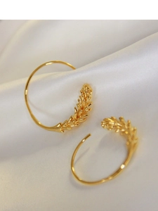 Detailed view of gold wheat ear earrings on white silk fabric with elegant curved hooks