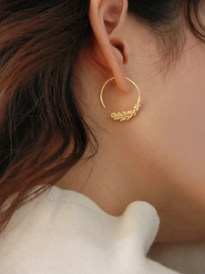 Detailed view of gold brass wheat ear drop earrings worn by a model in a natural setting