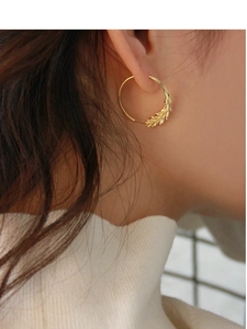 Close-up of gold-plated geometric wheat ear earrings worn by a model in soft light