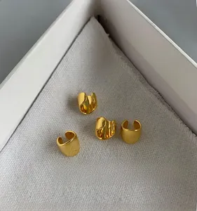 Close-up of four polished gold C-shaped ear cuffs on white textured fabric background