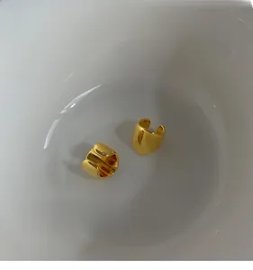 Detail of high-polished gold plated ear cuffs displayed in a white minimalist dish