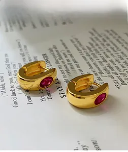 Detail view of gold C-shaped earrings with oval pink gemstones on vintage book pages