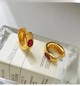 Close-up of vintage gold hoop earrings featuring an oval red zircon on a glass surface