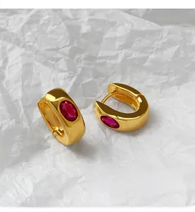 Close-up of gold U-shaped earrings with inlaid oval red zircon on white textured background
