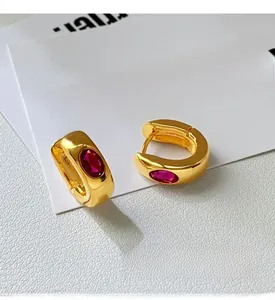 Close-up of vintage gold huggie earrings featuring inlaid red oval gemstones on white leather
