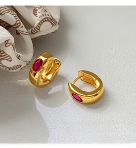 Close-up of gold hoop earrings with oval red gemstones on a luxury textured surface
